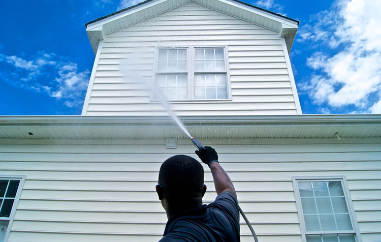 Man pressure washing home exterior