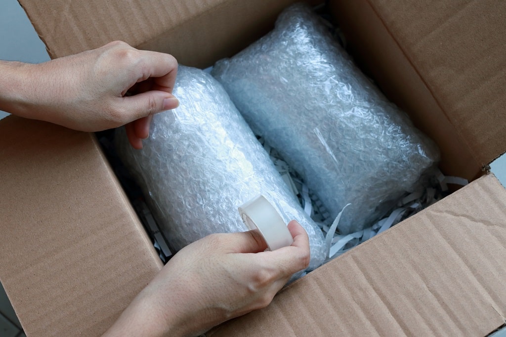 Hands packing fragile items in bubble wrap and paper inside a box for safe moving